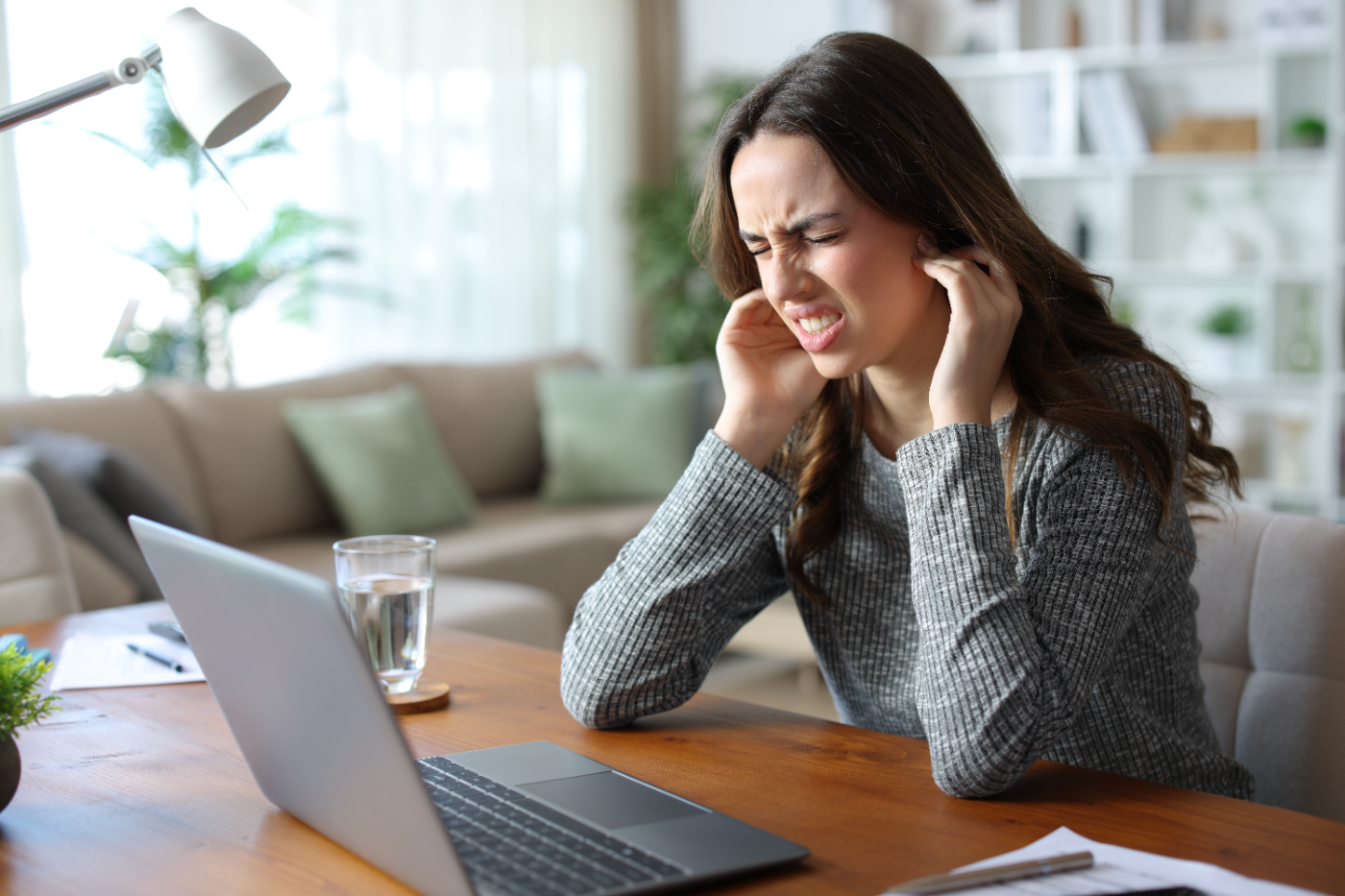 Woman at her desk holding her jaw in discomfort from TMJ pain, Root Cause Dental Group, London Ontario